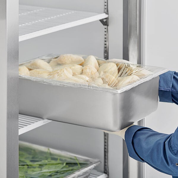 A person in blue gloves holding a Vollrath stainless steel tray of food.