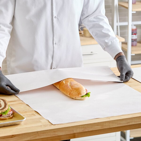 A person wrapping a sandwich with a large sheet of newsprint sandwich wrap paper on a wooden counter.