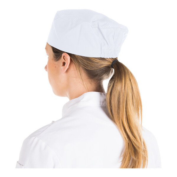 A person with long blonde hair tied in a ponytail is wearing a white cap and a white uniform, viewed from the back.