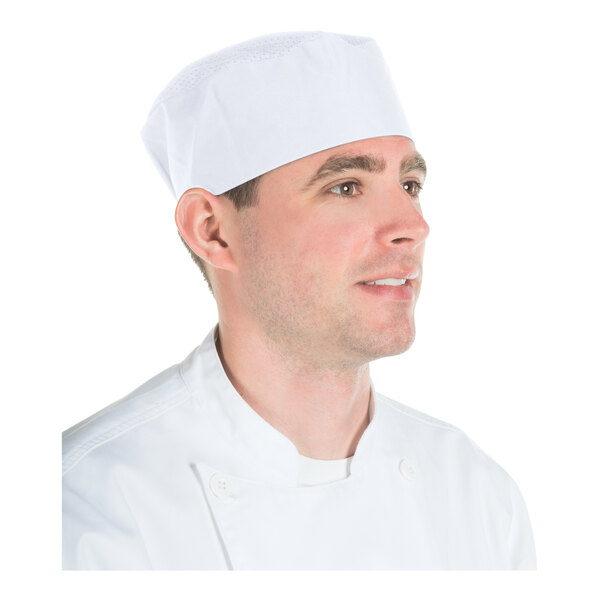 A man wearing a white chef's jacket and a white mesh-topped skull cap hat.