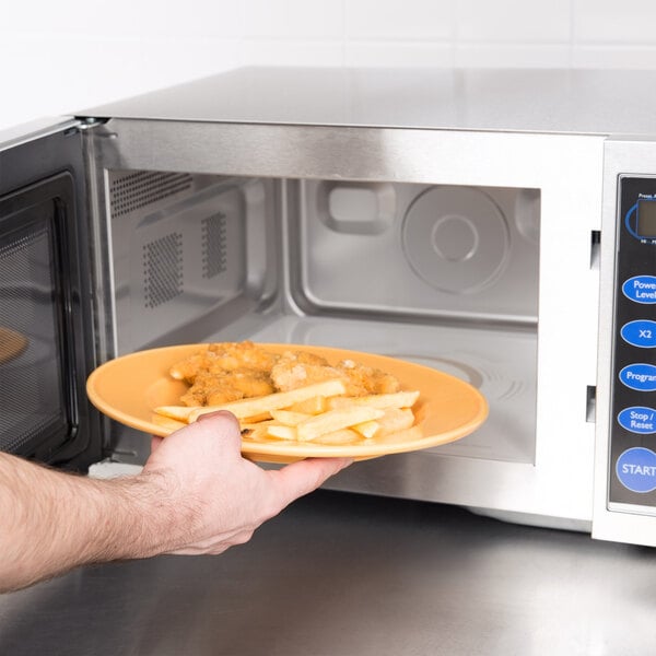 A person using a Vollrath commercial microwave to heat a plate of food.