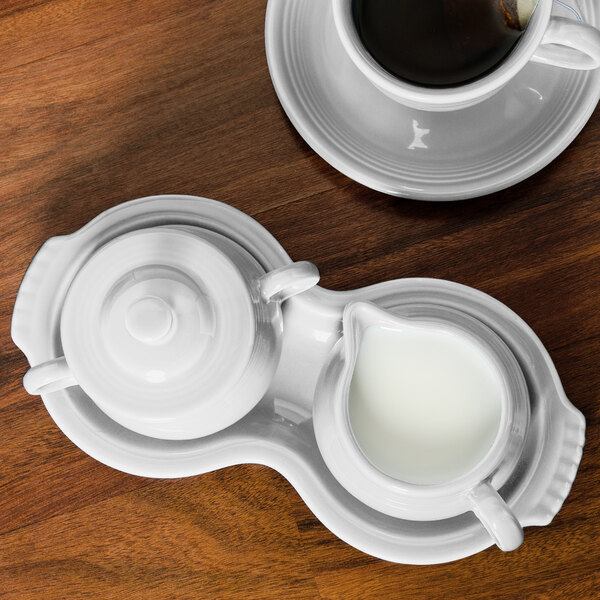 A white saucer with a creamer and a cup of coffee.