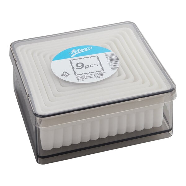 A clear plastic box containing a nested set of white, square-shaped cutters with fluted edges.