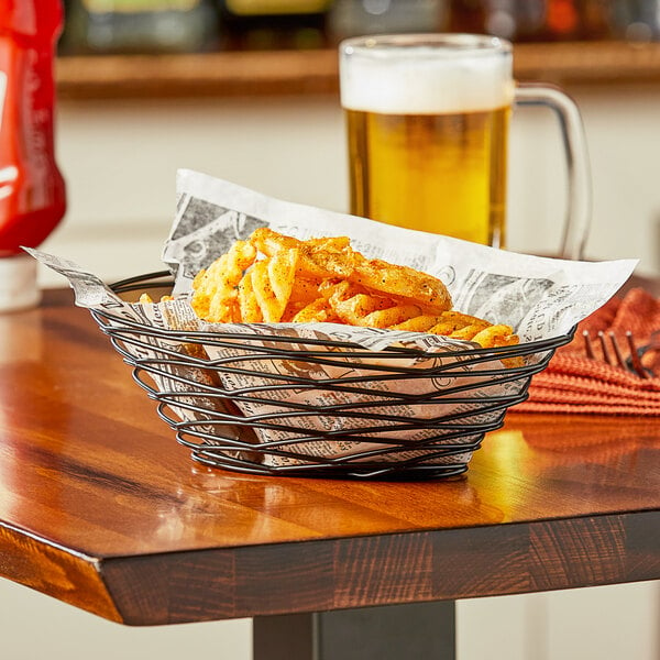 An American Metalcraft black oval basket of french fries on a table.