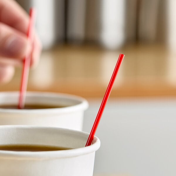 A red and white coffee stirrer placed in a paper cup filled with a hot beverage.