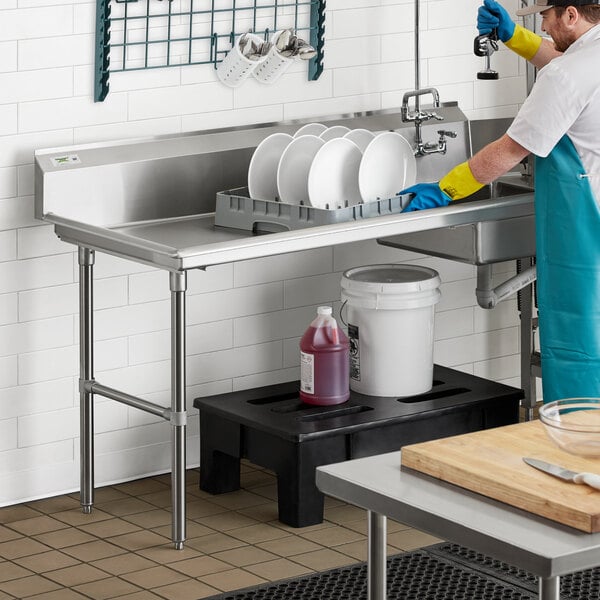 A man wearing blue gloves and an apron washing dishes in a Regency soiled dish table.