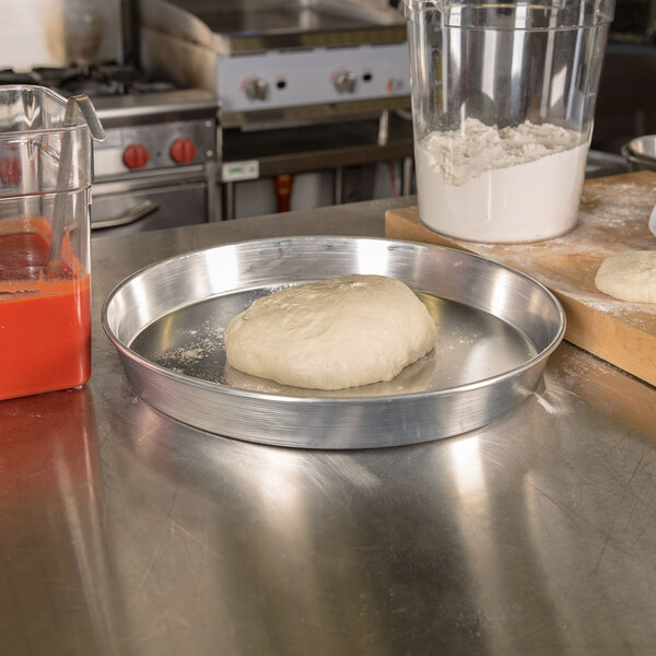 A ball of dough on an American Metalcraft aluminum pizza pan on a counter.