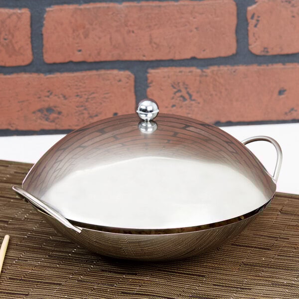 A silver stainless steel wok cover on a table.