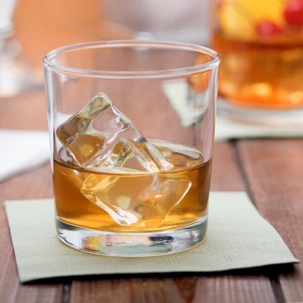 An Anchor Hocking Regency heavy base rocks glass filled with liquid and ice cubes on a napkin.