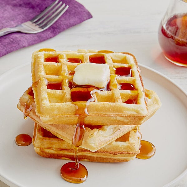 A stack of waffles with butter and syrup on a plate.