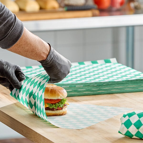 A sheet of green check deli sandwich wrap paper being used to wrap a sandwich.