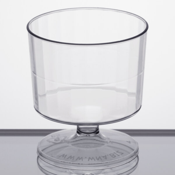 A WNA Comet clear plastic wine cup with a round pedestal on a white surface.