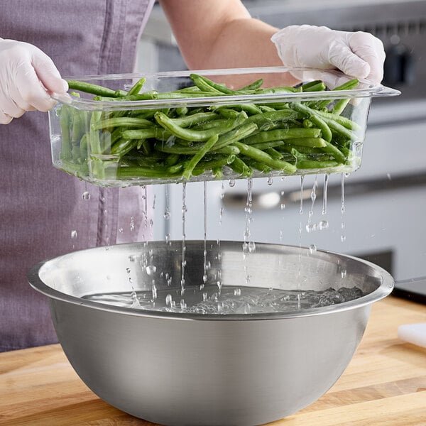 A woman using a Cambro clear colander pan to drain green beans.