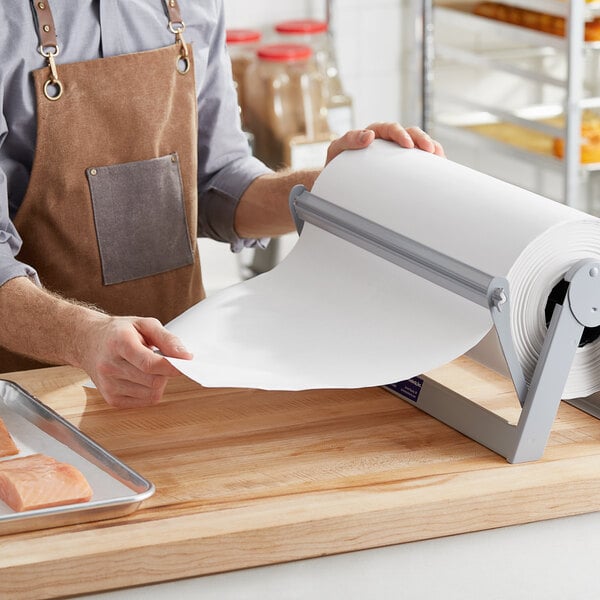 A person in an apron using a Choice White Economy Freezer Paper roll to cut paper.