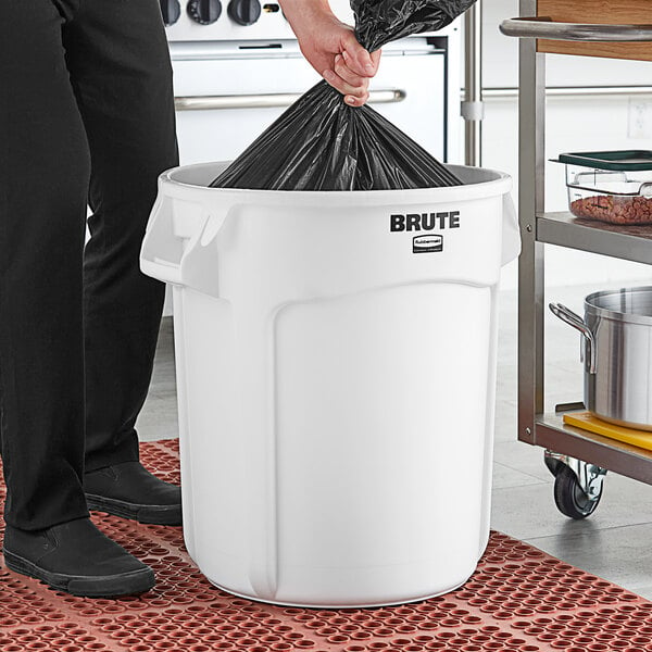 A person putting a black garbage bag into a white Rubbermaid utility trash can.