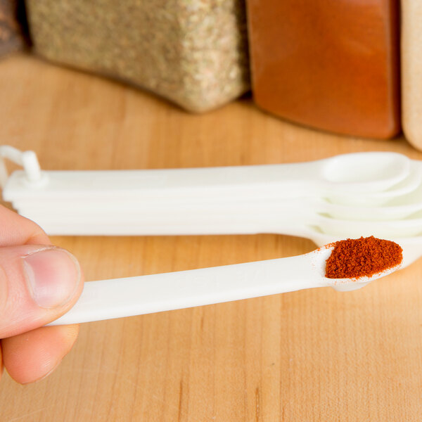 A person using a Rubbermaid white plastic measuring spoon to measure red spices.