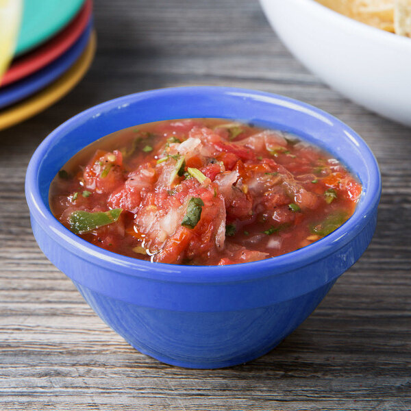 A peacock blue melamine bowl of salsa on a wood table.