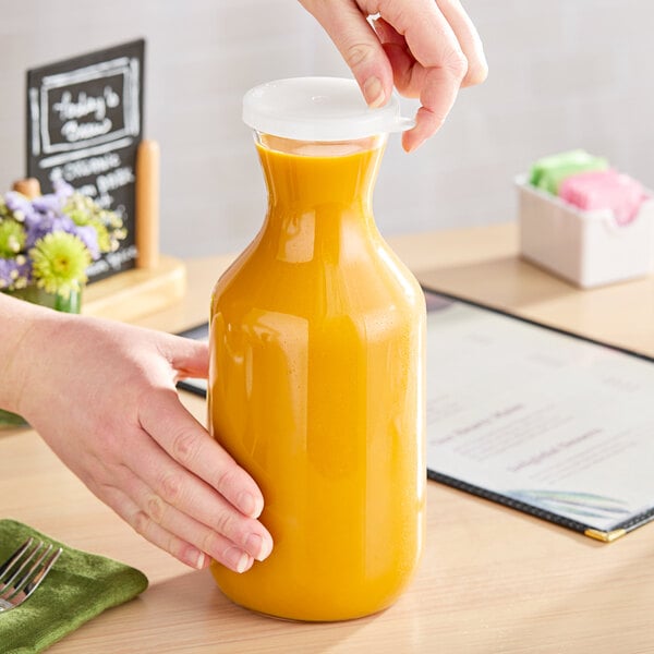 A person pouring orange juice from a Cambro Camliter decanter into a glass.