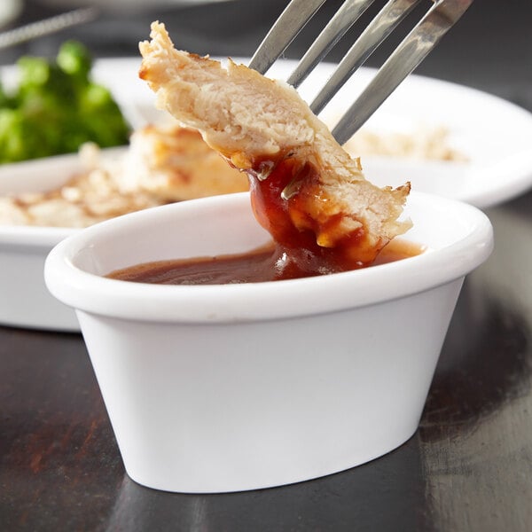 A fork with a piece of meat in white sauce in a white Carlisle ramekin.