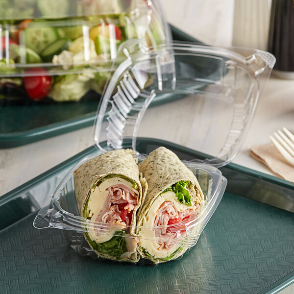 A clear plastic Dart hinged lid container holding a sandwich and a fork.