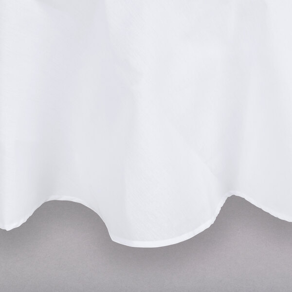 An Intedge white poly/cotton blend round table cover with hemmed edges on a table.