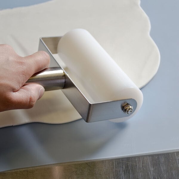 A person using an American Metalcraft stainless steel and plastic rolling pin to roll out dough.