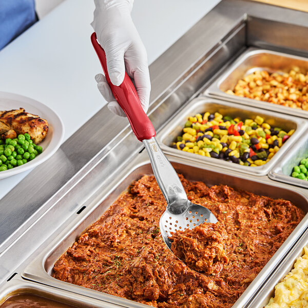 A person using a Vollrath Jacob's Pride heavy-duty perforated basting spoon with a red handle to serve food.