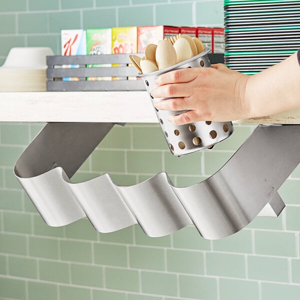 A hand holding a Steril-Sil stainless steel flatware organizer full of spoons.