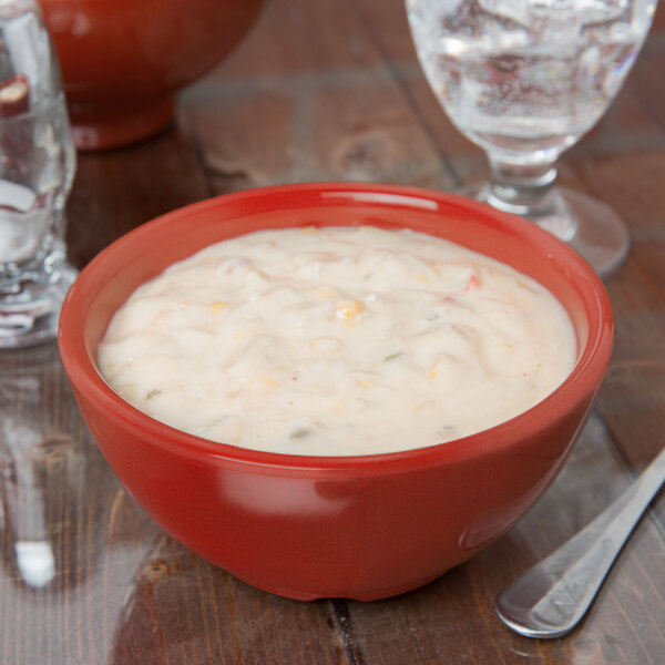 A red Diamond Harvest cranberry melamine bowl filled with soup on a table with a glass of water.