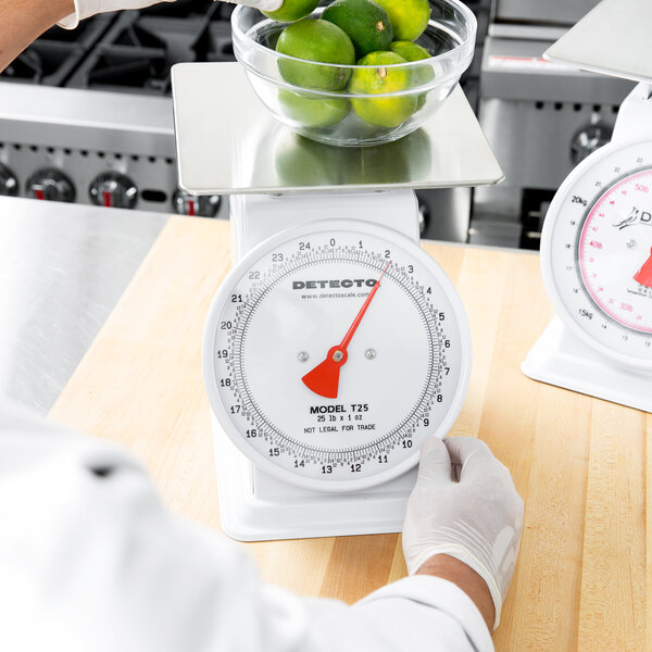 A person weighing a bowl of limes on a Cardinal Detecto portion scale.