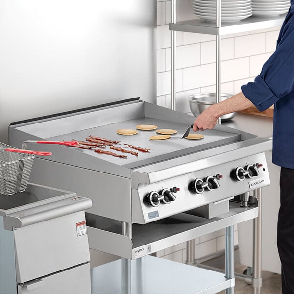A stainless steel 36-inch natural gas countertop griddle with thermostatic controls, shown cooking bacon and pancakes in a commercial kitchen setting.