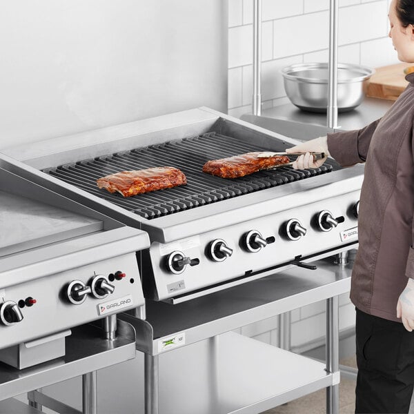 A woman cooking ribs on a Garland gas charbroiler with adjustable grates.