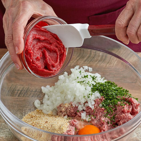 A person holding a spoon in a bowl of red paste.