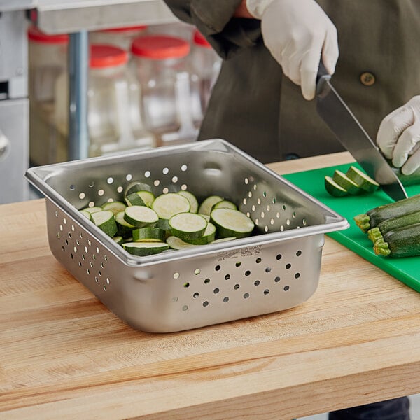 A person cutting cucumbers in a Vollrath stainless steel steam table pan.