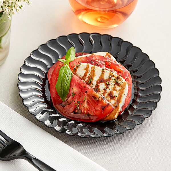 A Fineline Flairware black plastic plate with cheese and tomatoes on it.