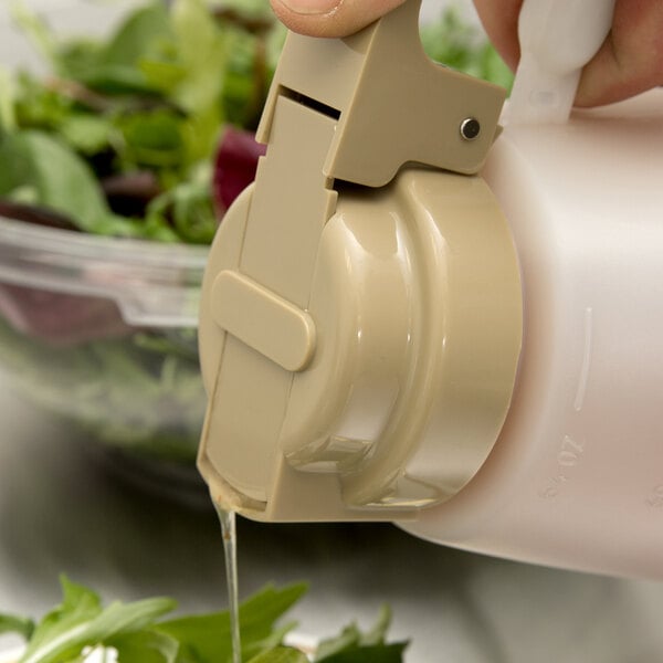 A hand pouring dressing from a Tablecraft beige dressing top onto a salad.
