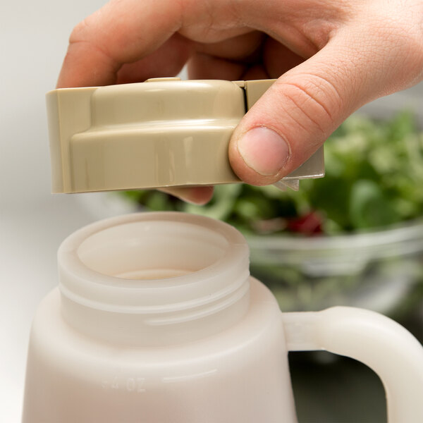 A hand using a Tablecraft beige dressing top on a plastic container.