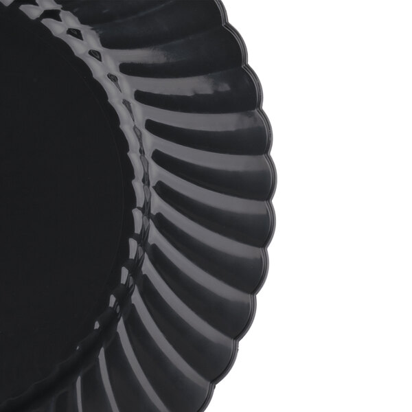 A close-up of a black WNA Comet Classicware EcoSense plastic plate with a scalloped edge.