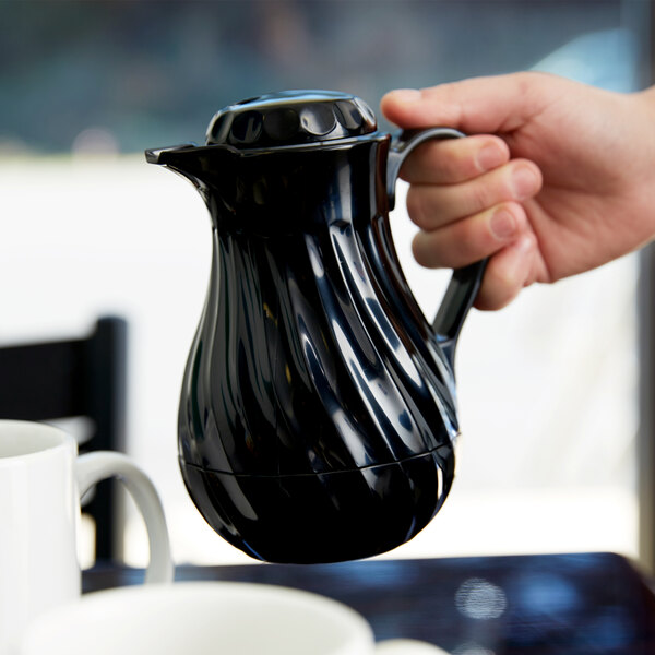 A hand holding a black Vollrath SwirlServe coffee server filled with a hot beverage.