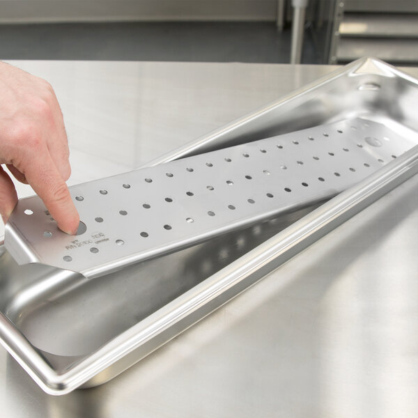 A person's hand holding a Vollrath stainless steel false bottom over a metal tray.