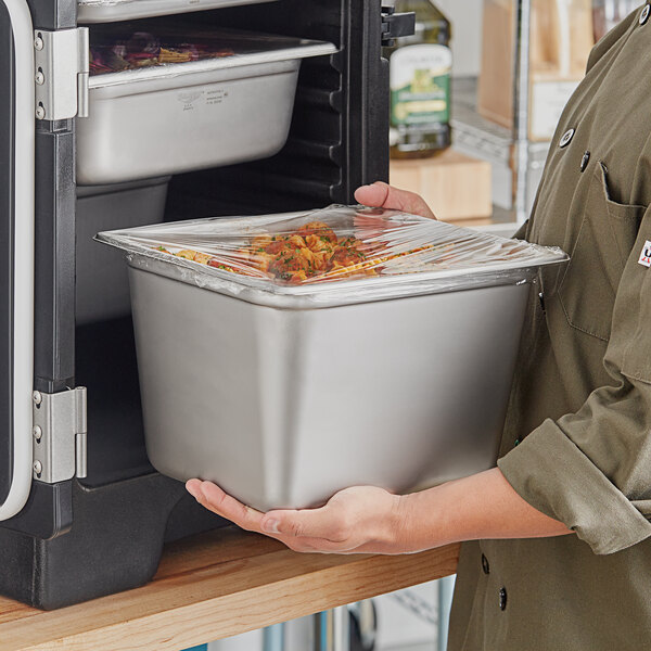 A man holding a Vollrath stainless steel transport pan full of food at a catering event.
