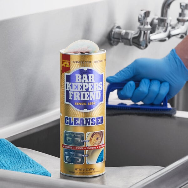 A canister of Bar Keepers Friend 21 oz. all-purpose cleaning powder placed on a stainless steel sink.