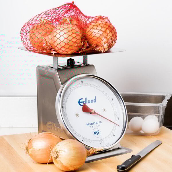 An Edlund heavy-duty portion scale on a counter with onions in a red net.