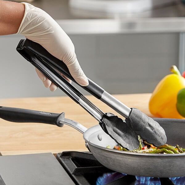 A person using Vollrath Jacob's Pride tongs with a black handle to cook over a pan.