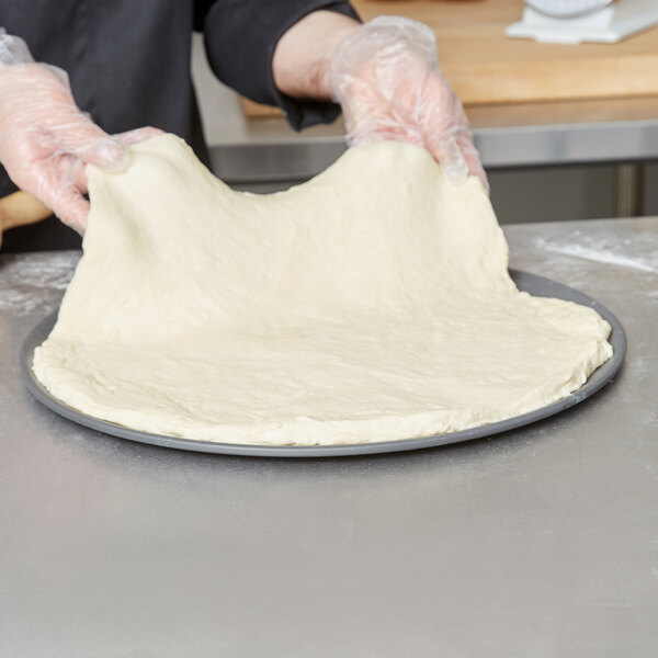 A person in gloves holding pizza dough over an American Metalcraft Super Perforated Pizza Pan.