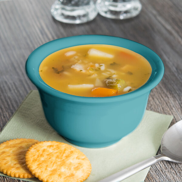 A Fiesta turquoise China bouillon bowl filled with soup with a spoon and crackers on a napkin.
