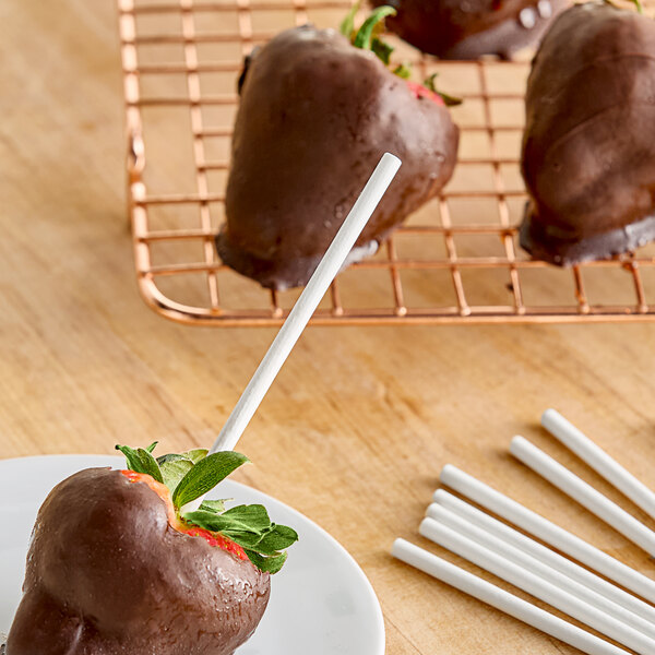 Chocolate covered strawberries on a plate with white cake pop sticks.