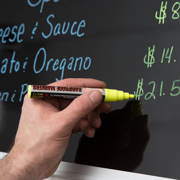 Person writing on a black menu board with a yellow rainproof marker