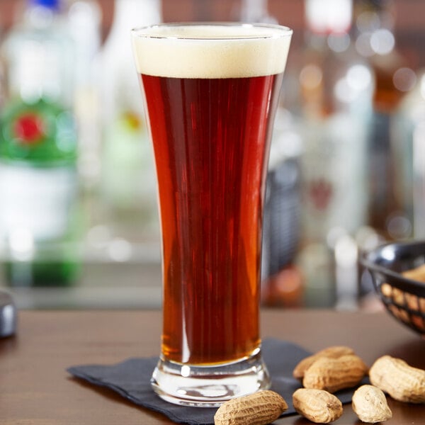 A close up of a glass of Anchor Hocking beer with a few peanuts on a table.