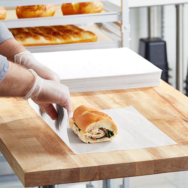 A person cutting a sandwich on dry wax paper.